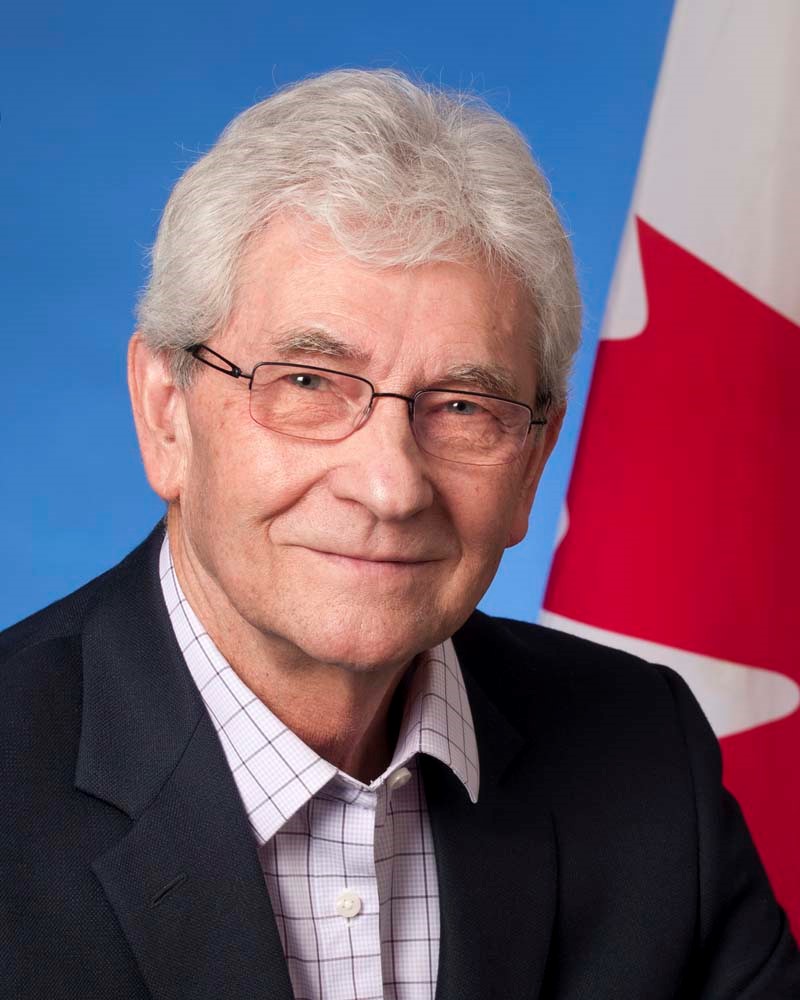 A colour photo of Dennis Gruending with Canada's red and white maple leaf flag in the background. 