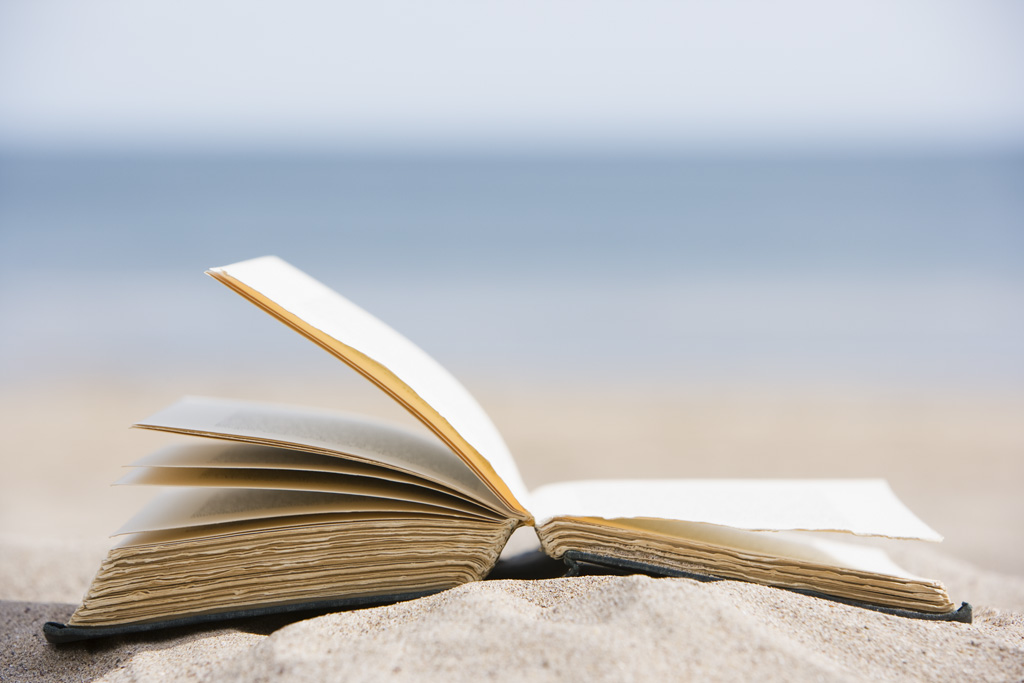 Photo of open book on a sandy beach.